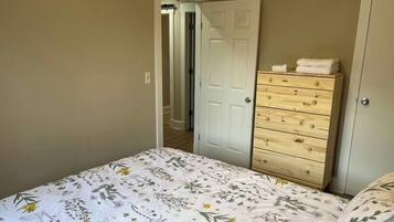 Quarto com uma cama, cômoda de madeira e porta que dá para outro ambiente.