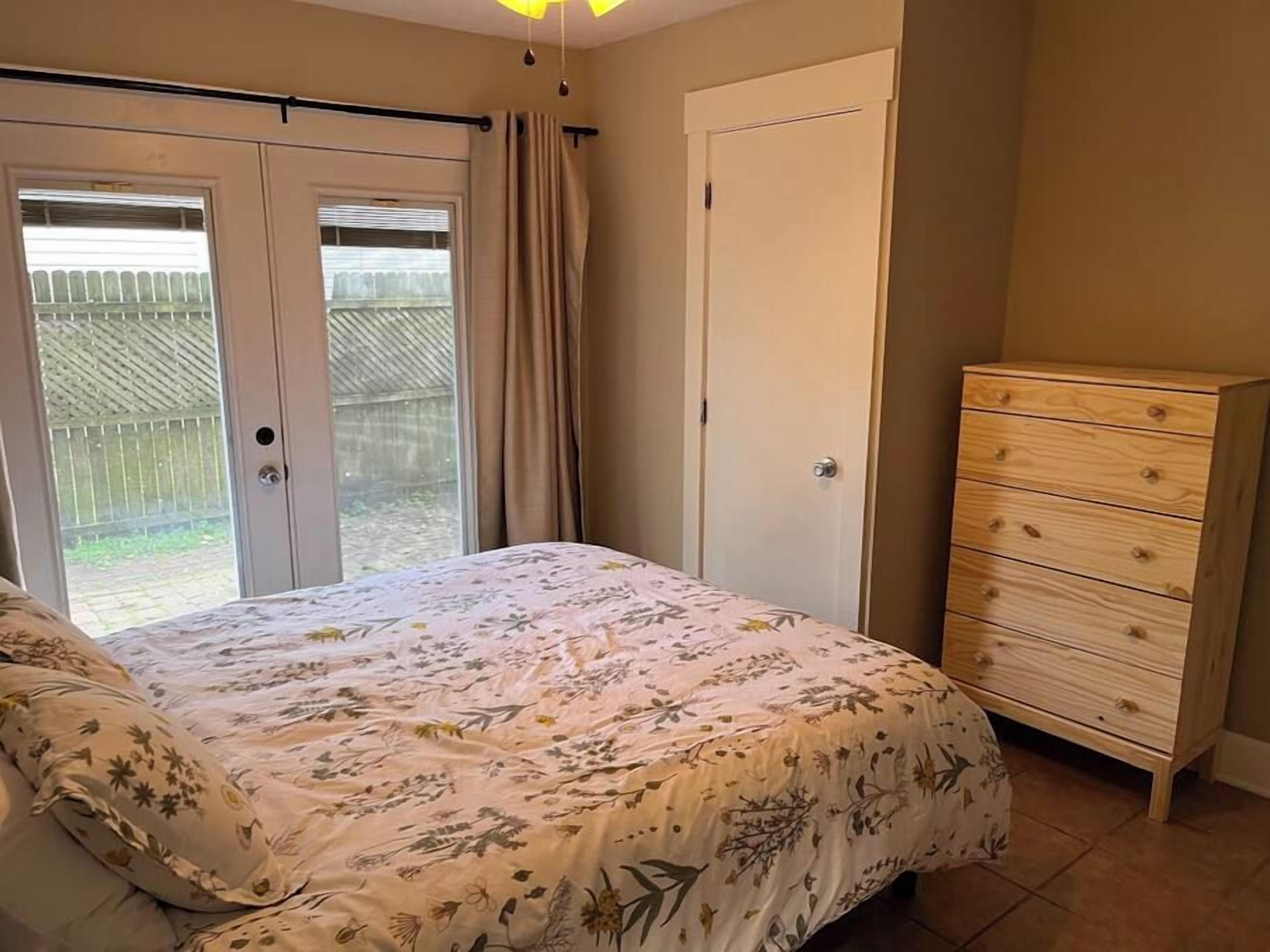 Une chambre à coucher comprenant un lit, une commode et une porte-fenêtre coulissante donnant sur un balcon.