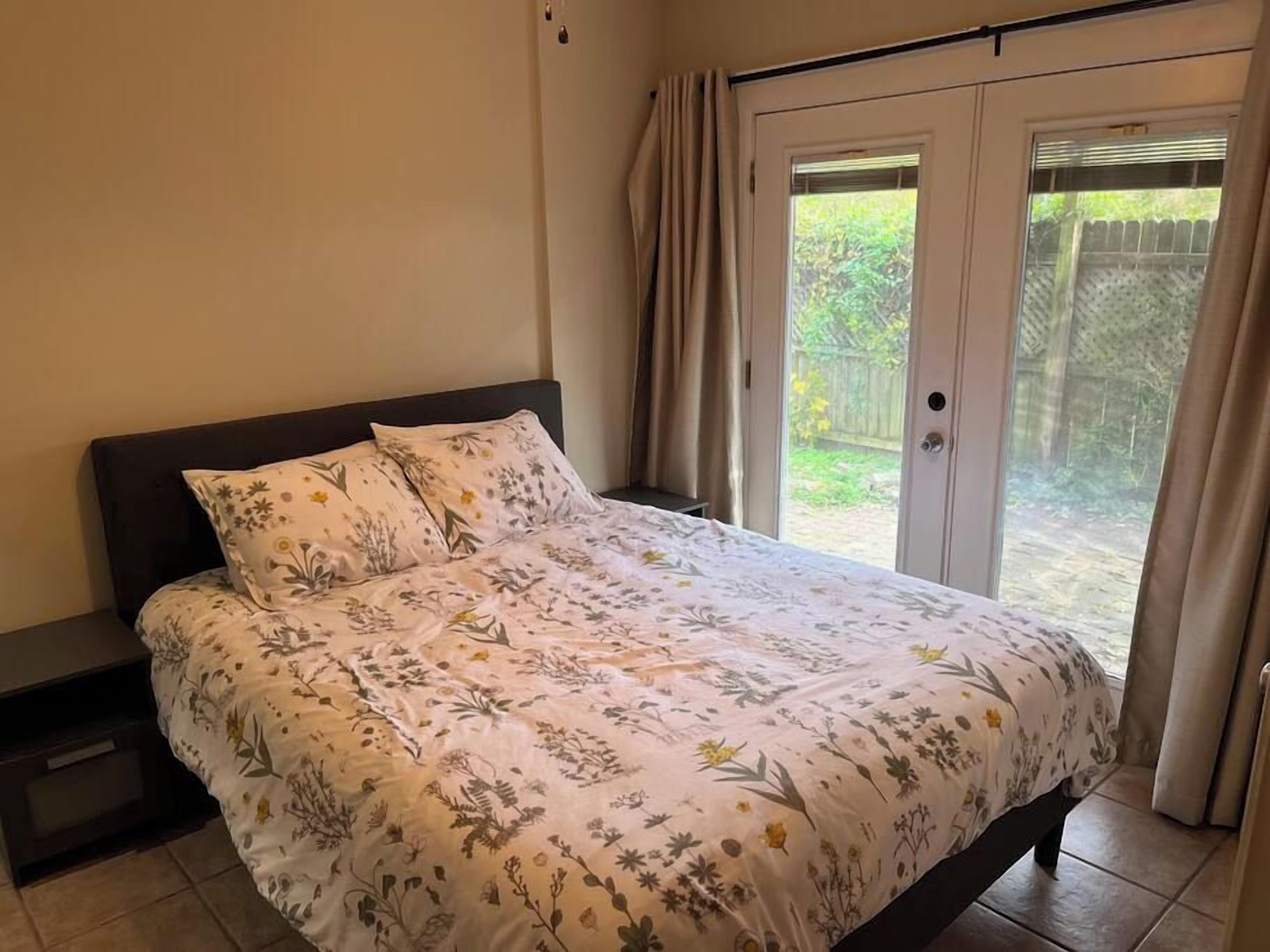 Ein Schlafzimmer mit einem Bett, einem Nachttisch und einer Schiebetür, die in einen Garten führt.