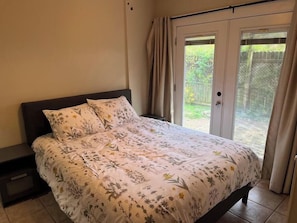 A bedroom with a bed, a nightstand, and a sliding glass door leading to a garden.