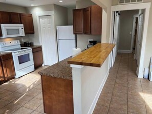 A kitchen with a wooden countertop, white cabinets, a microwave, an oven, and a refrigerator.