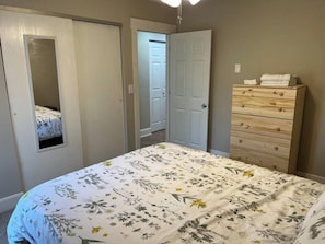 A bedroom with a bed, a dresser, and a door leading to another room.