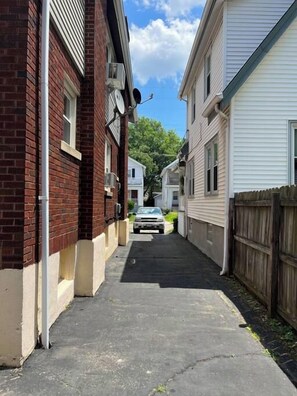 Eine schmale Wohnstraße mit Häusern aus Backstein und Weißputz, einem geparkten Auto und einem Holzzaun.