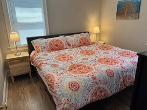 A bedroom with a bed, two bedside lamps, a nightstand, and a window with blinds.