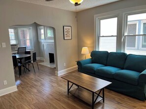 A living room with a green sofa, a wooden coffee table, and a dining area with a table and chairs.
