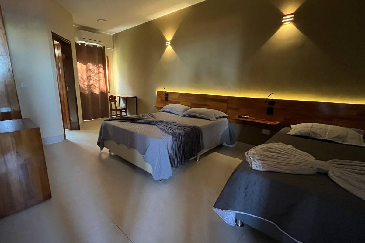A hotel room with two beds, a wooden headboard, a bedside table with a lamp, and a chair.