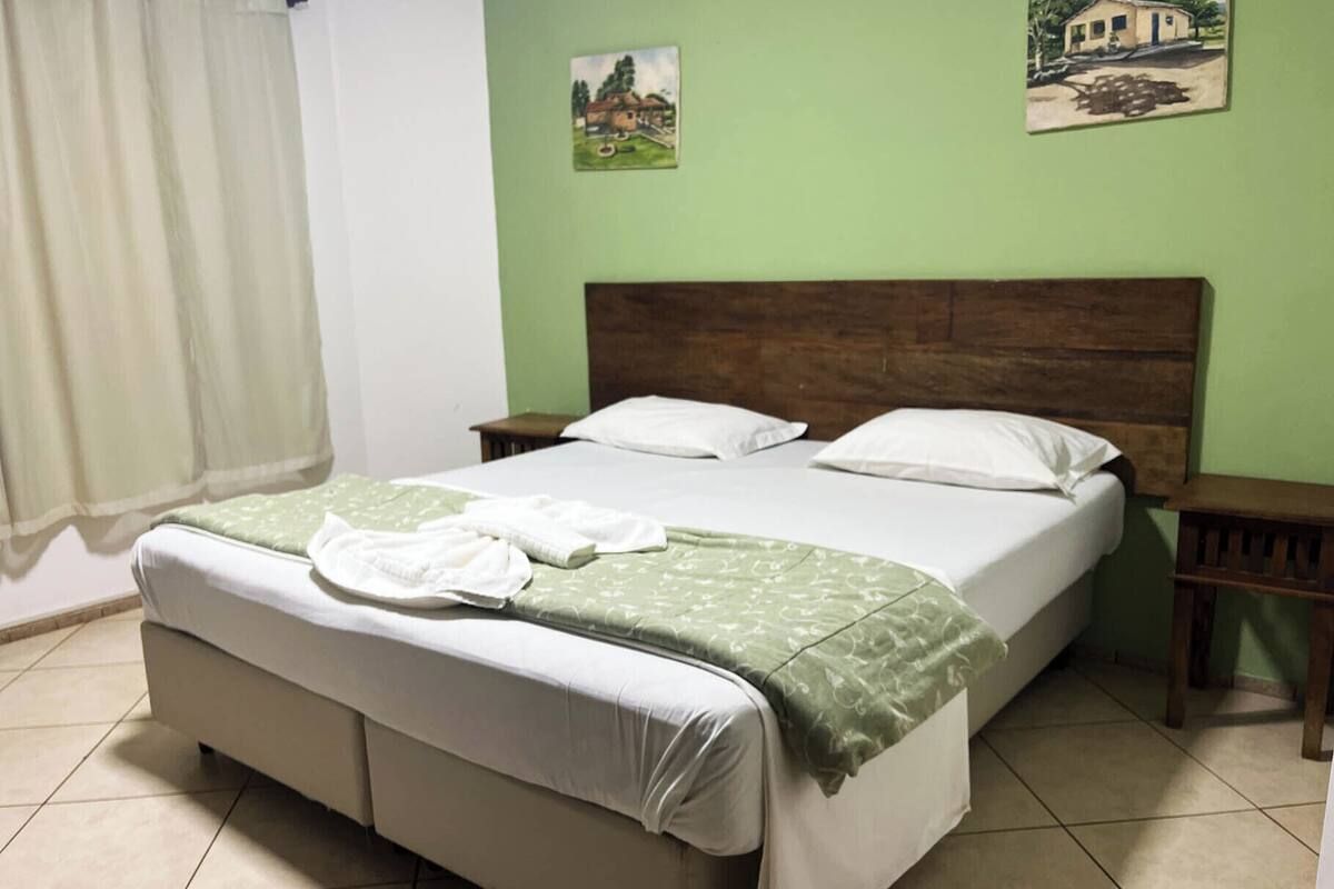 A single-bed room with a wooden headboard, a green patterned bedspread, and two white pillows.