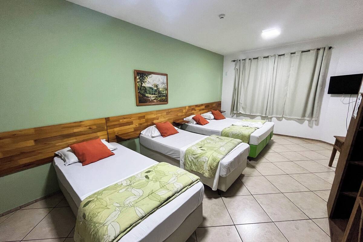 A hotel room with three single beds, a wooden headboard, a painting on the wall, and a TV mounted on the wall.