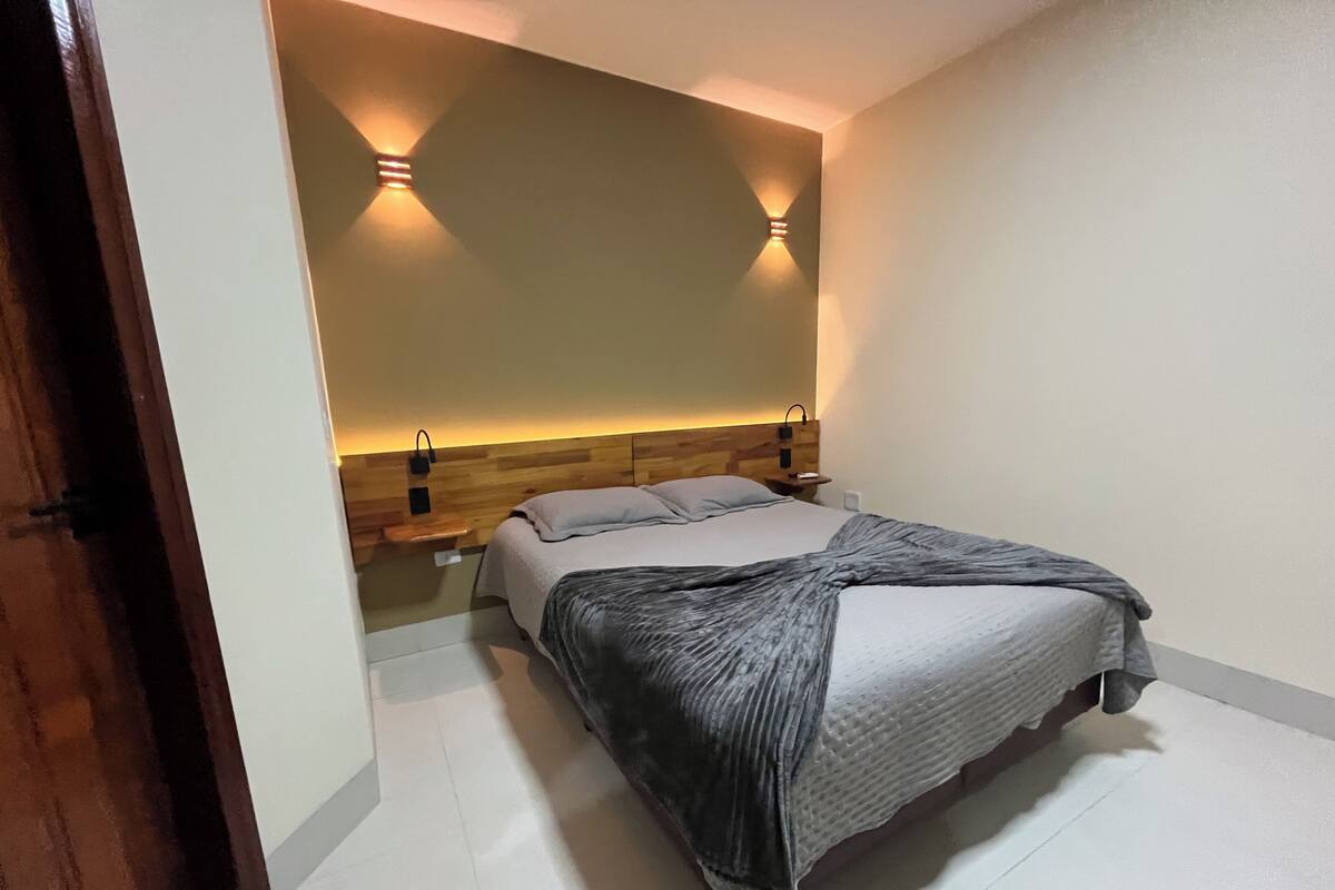 A bedroom with a bed, bedside tables, and wall-mounted lighting.