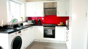 A modern kitchen with white cabinets, a black oven, and a red backsplash. - New Build Dickins Heath (Solihull)