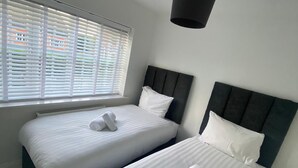 A hotel room with two beds, white bedding, a window with blinds, and a black pendant light. - New Build Dickins Heath (Solihull)