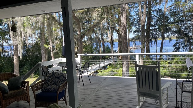 Une terrasse couverte, aménagée avec du mobilier d’extérieur, dotée d’une rambarde et offrant une vue sur l’eau et les arbres.