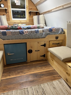 A cozy, compact bedroom with a built-in bed, a small wardrobe, and a window with a view of the outside.