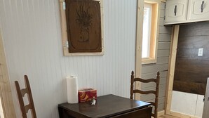 A dining area with a wooden table and chairs, a wall-mounted picture, and a window with a view of the outside. - Cozy Cabin (Clancy)