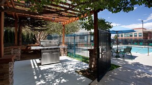 Un patio exterior con una parrilla, piscina y zona de estar techada.