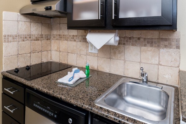 A kitchen with granite countertops, a stainless steel sink, a dish rack, and a dish soap bottle.