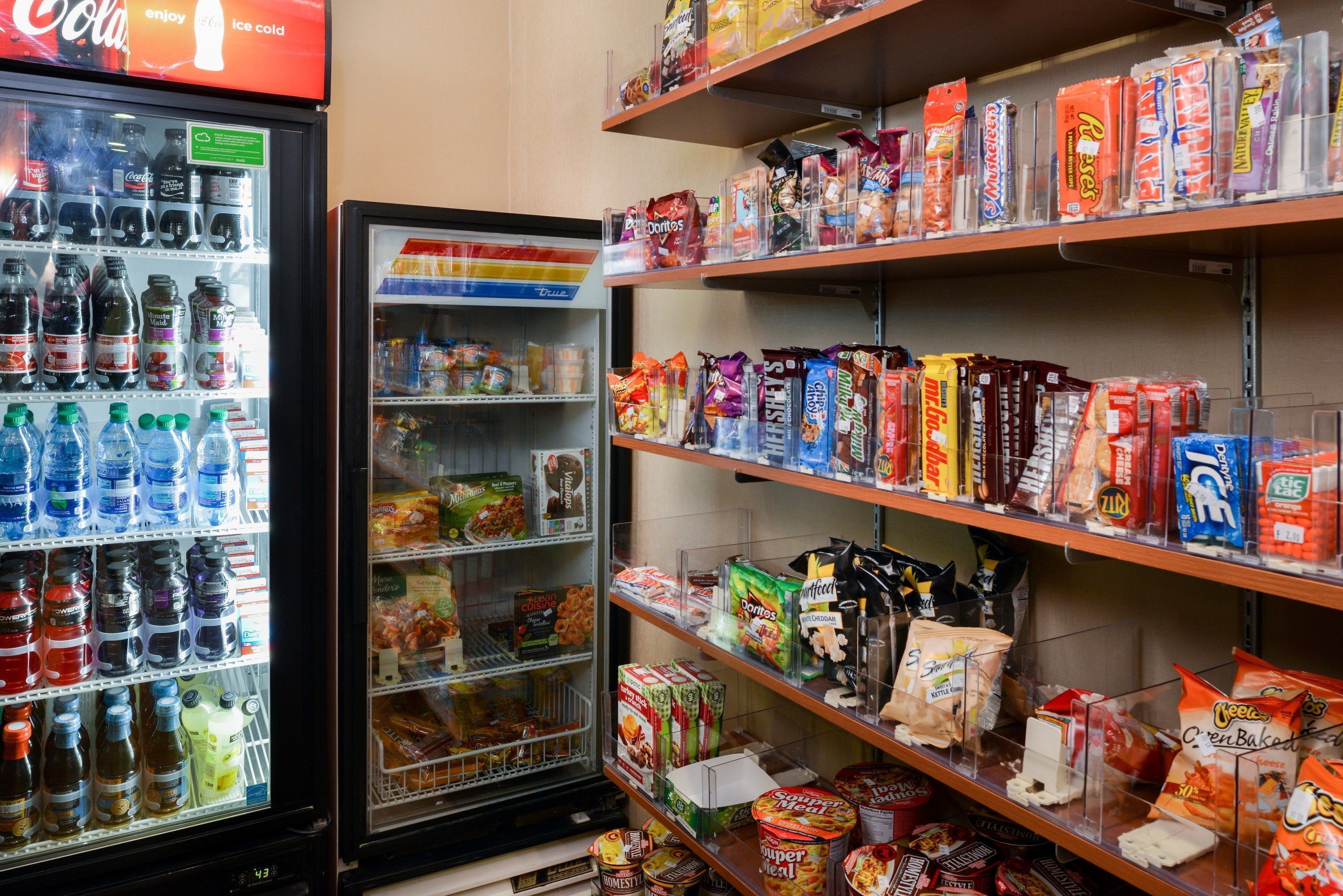 Mostrador refrigerado de bebidas y estantes con aperitivos y productos envasados.