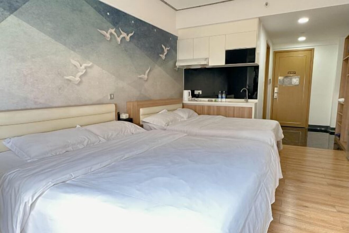 A hotel room with two beds, a kitchenette, a wall with a bird mural, and a wooden floor.