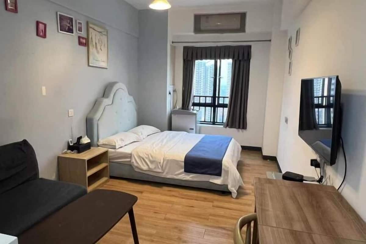 A bedroom with a bed, a desk, a chair, a TV, and a window with curtains.