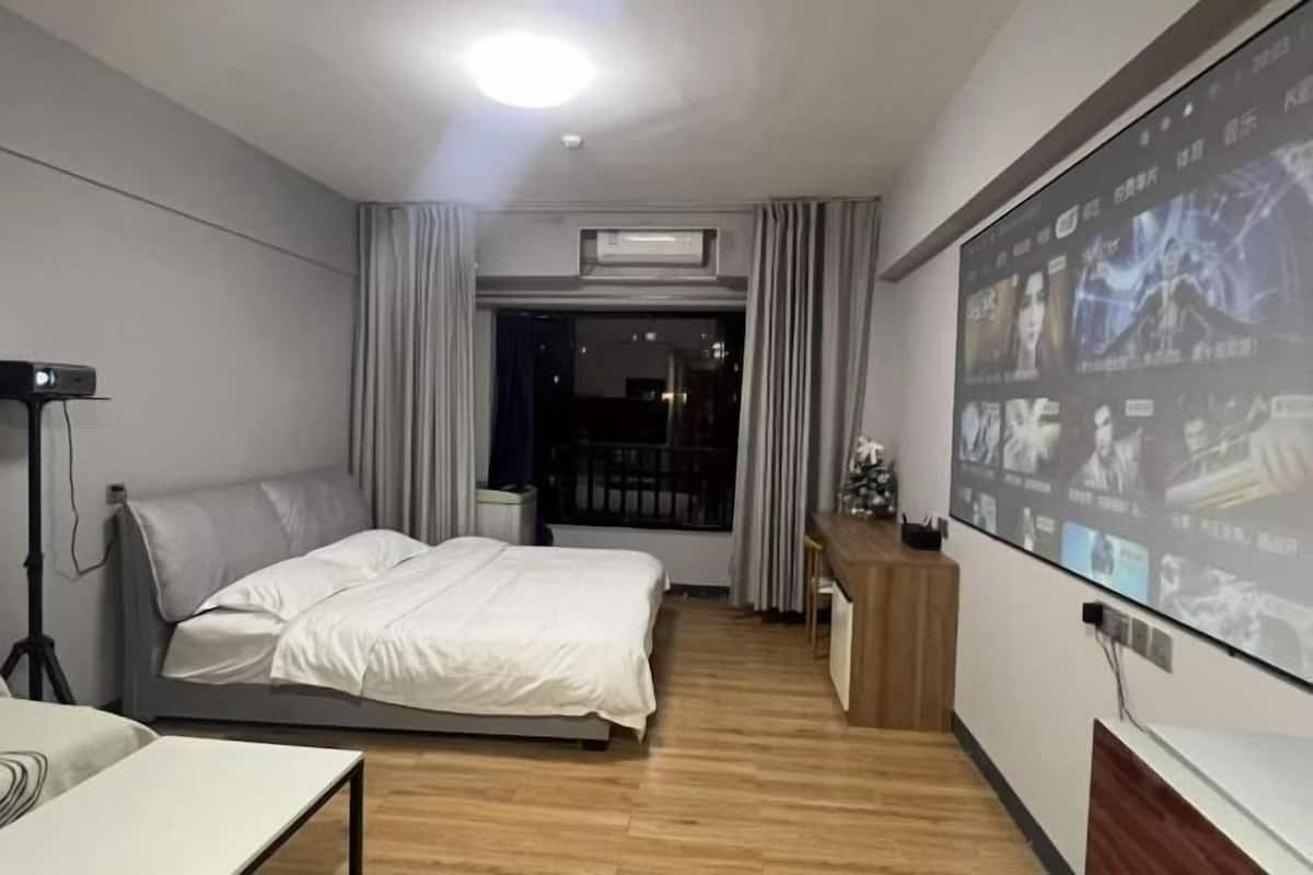 A hotel room with a bed, a desk, a projector screen, and a window with curtains.