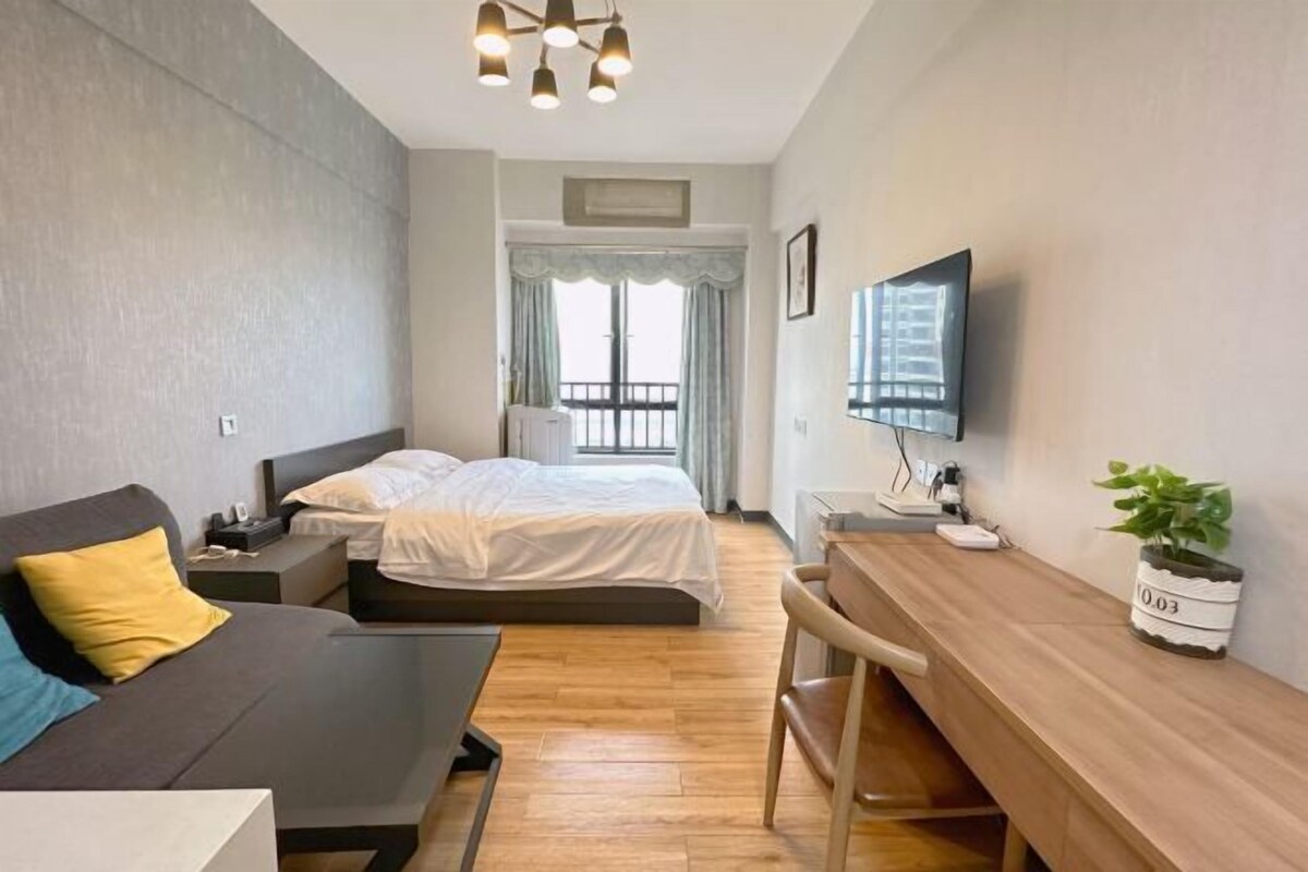 A bedroom with a bed, bedside table, lamp, TV, and a desk with a chair.