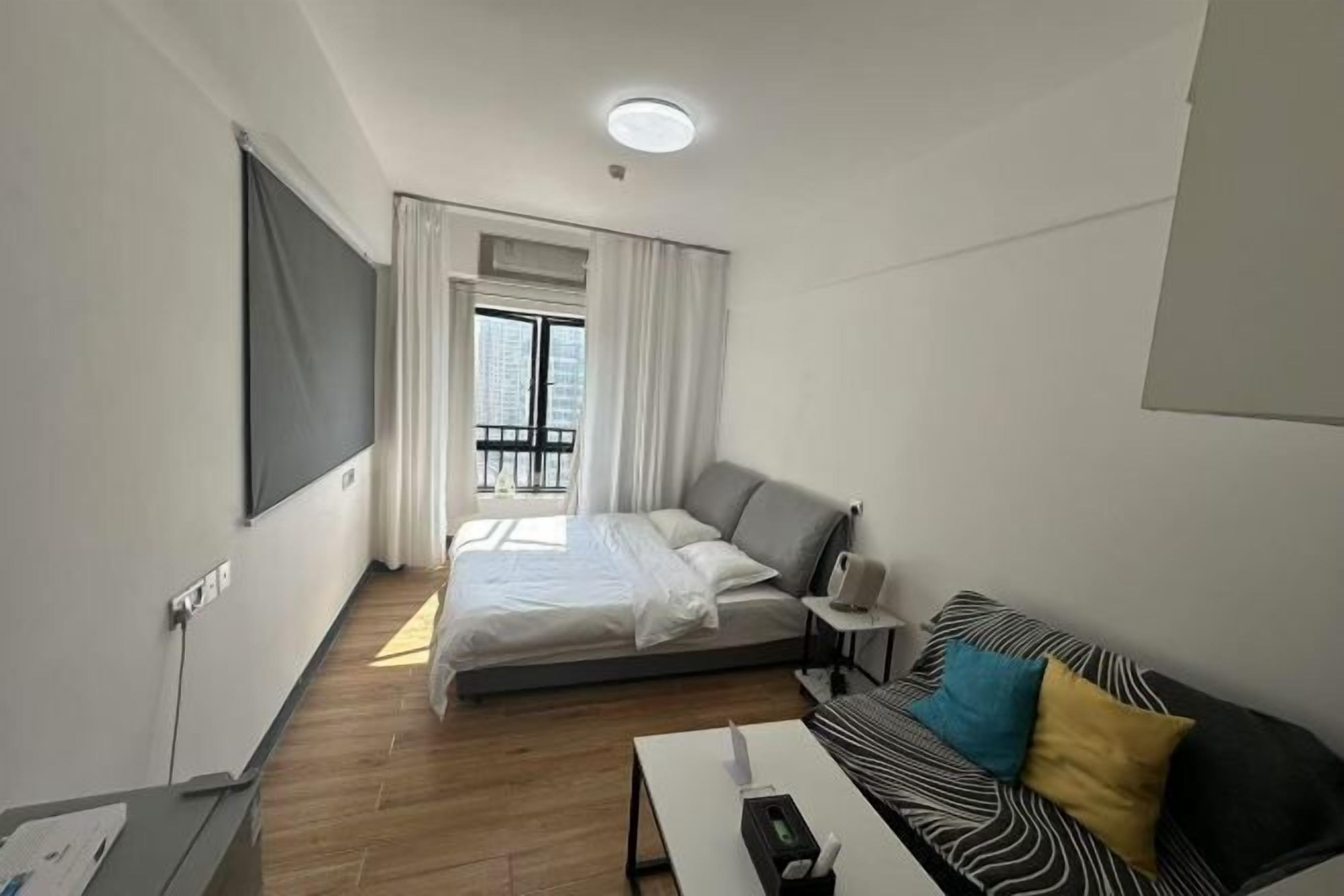 A hotel room with a bed, a sofa, a TV, a small table, and a window with curtains.