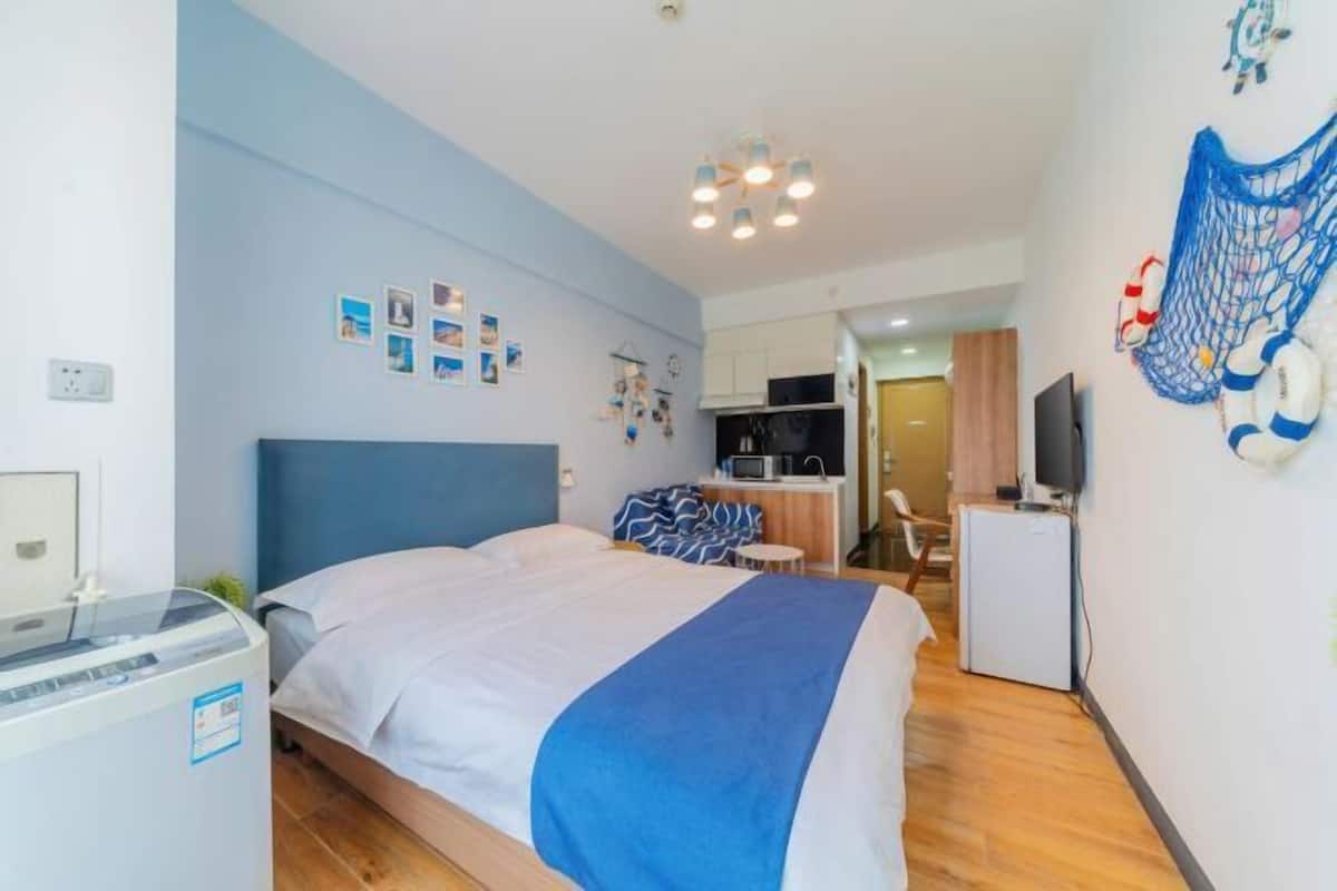 A compact hotel room with a bed, a small kitchenette, a TV, and a heater.