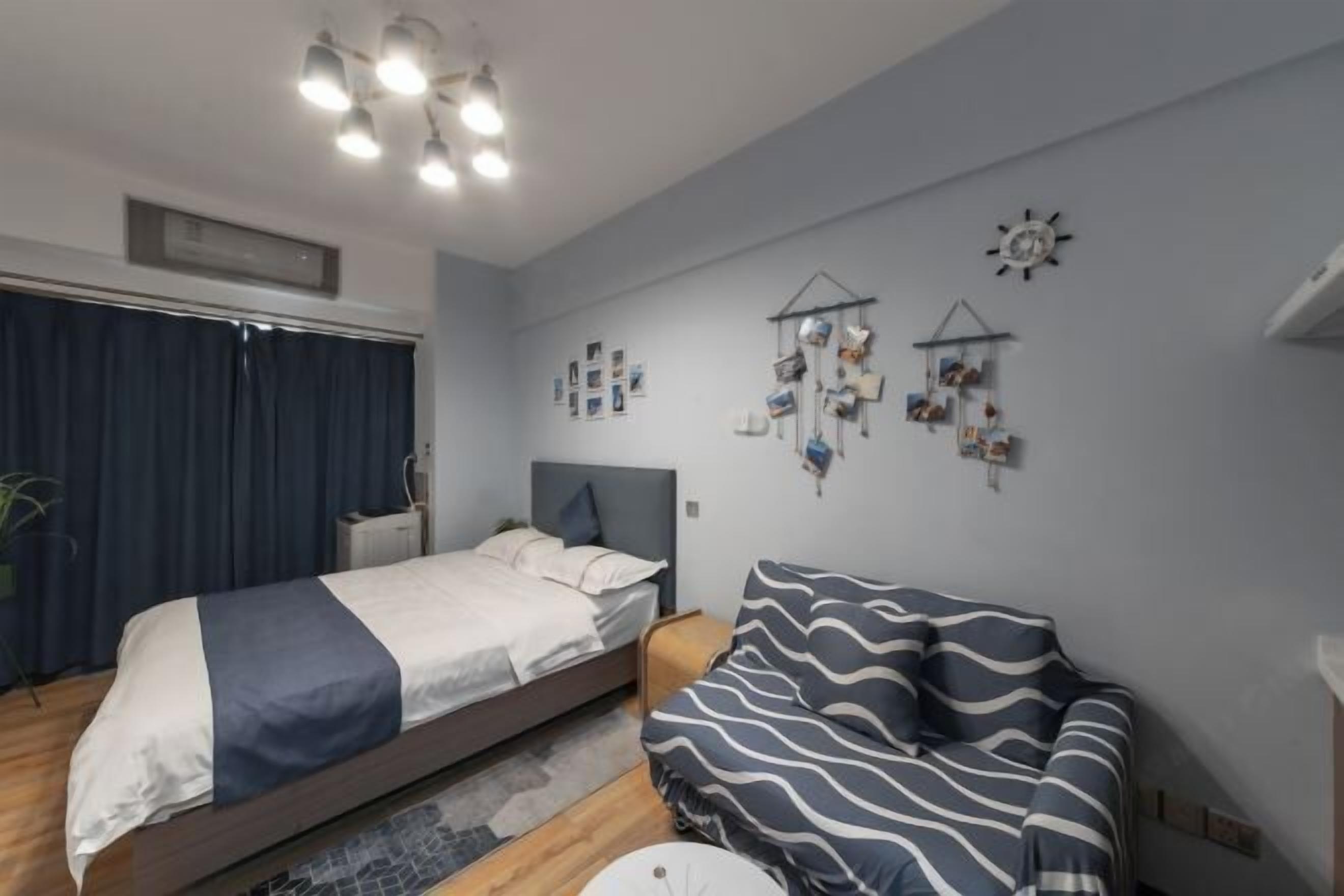 Un dormitorio con cama, sofá, lámpara de techo, reloj de pared y una pequeña estantería con diversos objetos.