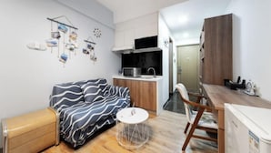 A compact living space with a kitchenette, a sofa, a small round table, and a wooden cabinet. - Best Apartment (Dongguan Huixing Square) (Dongguan)