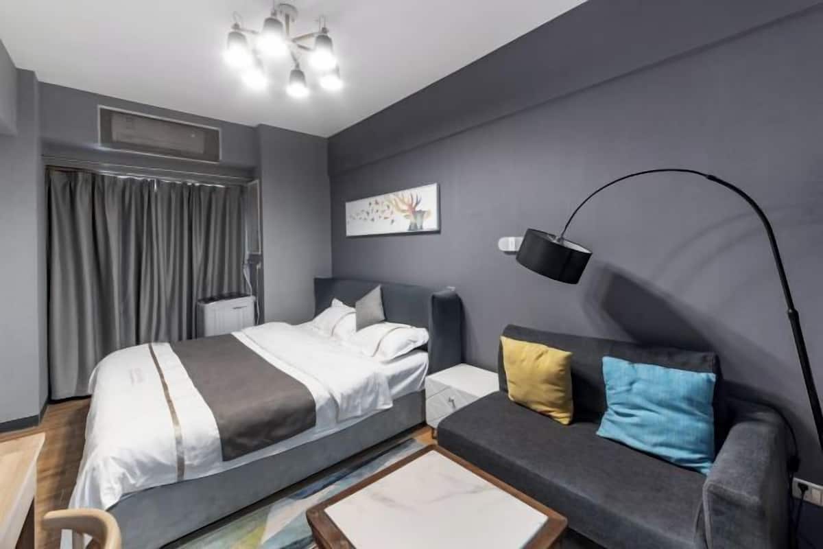 A modern bedroom with a bed, a sofa, a floor lamp, and a painting on the wall.
