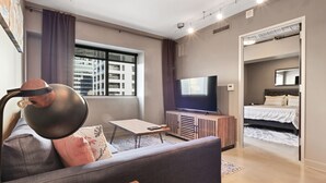 A modern living room with a sofa, a coffee table, a TV on a wooden cabinet, and a large window with curtains. - Luxurious 1 Bedroom Condo in Downtown Austin (Austin)