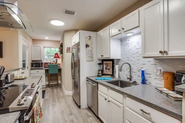 A modern kitchen with white cabinetry, a stainless steel refrigerator, a microwave, and a sink.