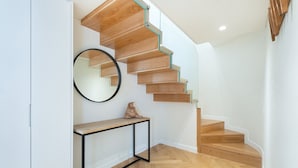 A modern staircase with wooden steps and glass railings, a round mirror, and a small console table with a sculpture. - GuestReady - Modern and exquisite apt near Estrela (Lisbon)
