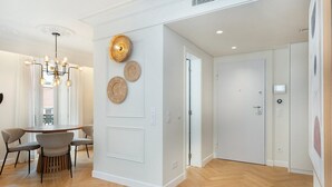 A modern interior with a dining area, a chandelier, and a hallway leading to a door. - GuestReady - Modern and exquisite apt near Estrela (Lisbon)