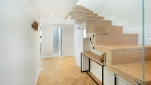 A modern staircase with wooden steps and glass railings, leading to an interior space with a wooden floor and white walls. - GuestReady - Modern and exquisite apt near Estrela (Lisbon)