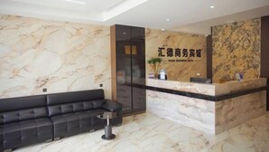 A hotel reception area with a marble wall, a black sofa, and a reception desk. - OYO Ulanhot Huide Business Hotel (Ulanhot)