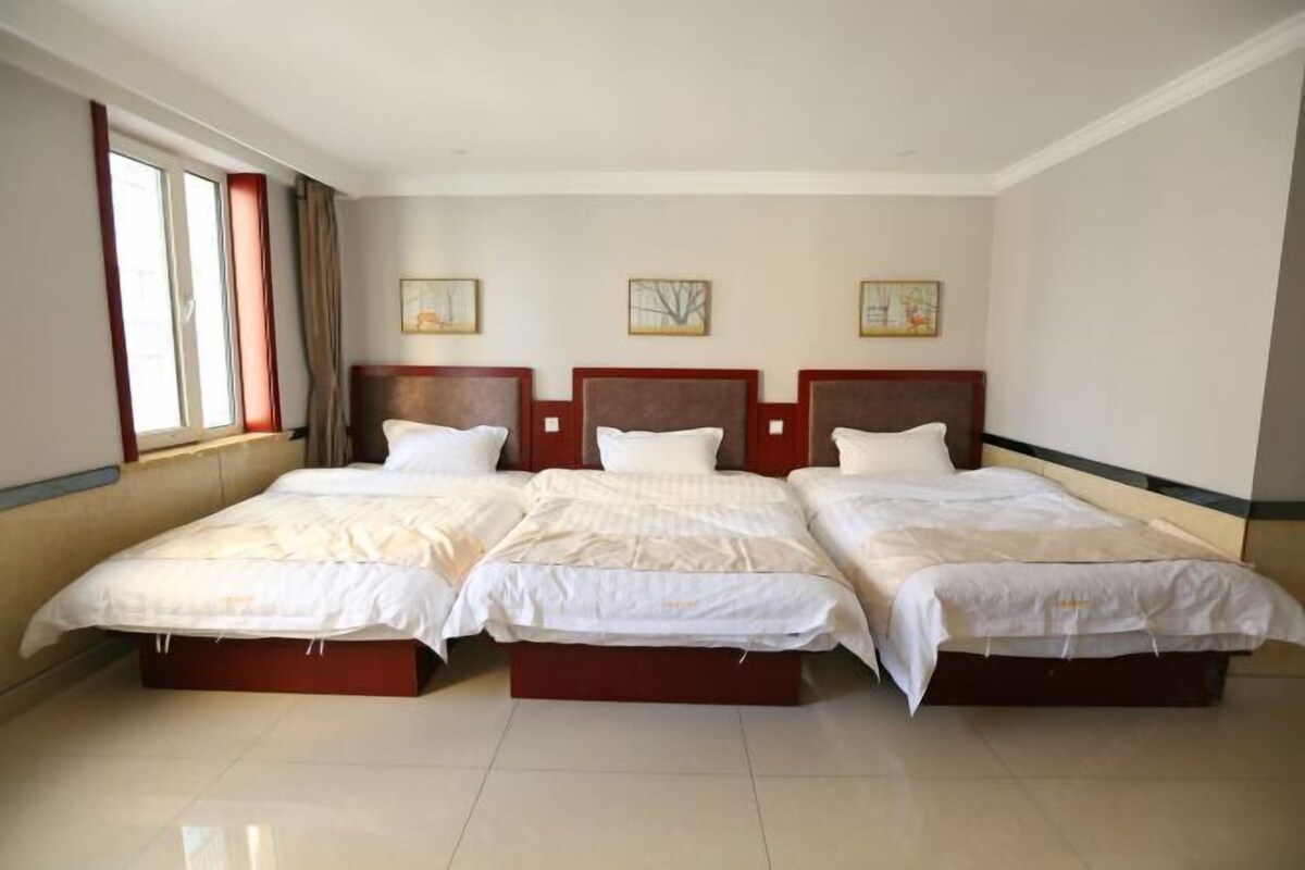 A hotel room with three beds, a large window with curtains, and artwork on the walls.