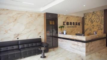 A hotel reception area with a marble wall, a black sofa, and a reception desk.