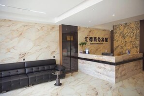 A hotel reception area with a marble wall, a black sofa, and a reception desk. - OYO Ulanhot Huide Business Hotel (Ulanhot)