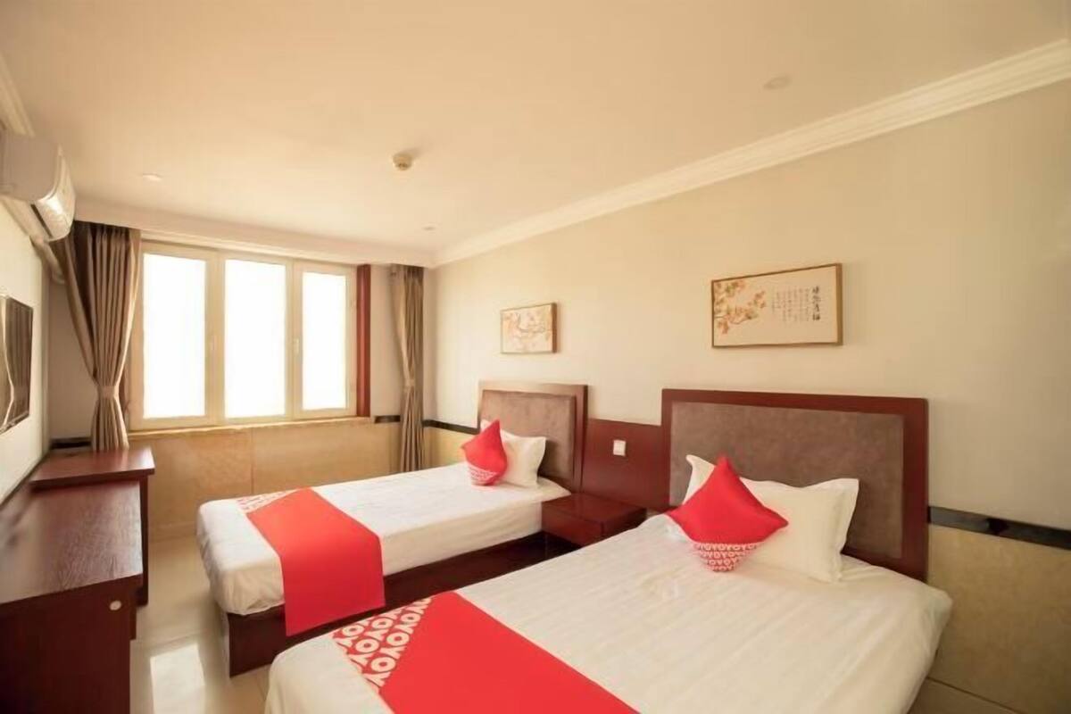 A hotel room with two beds, a desk, and a window with curtains.