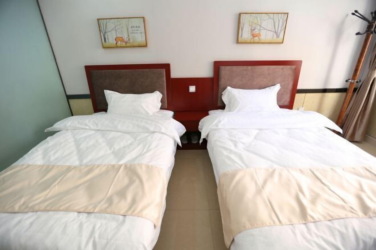 A hotel room with two single beds, a wooden headboard, a small table, and two framed pictures on the wall.