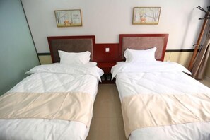 Quarto de hotel com duas camas de solteiro, cabeceira de madeira, uma mesa pequena e duas imagens emolduradas na parede.