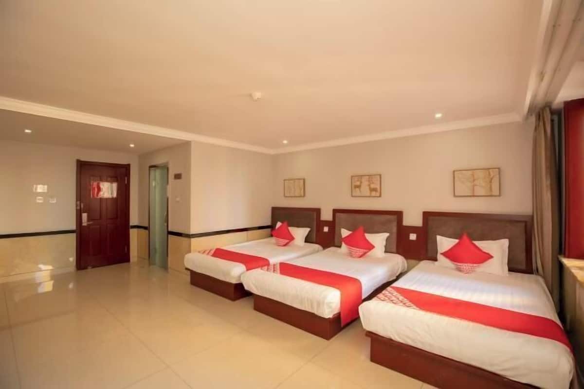 A hotel room with three beds, each with a red and white bedspread and matching pillows.
