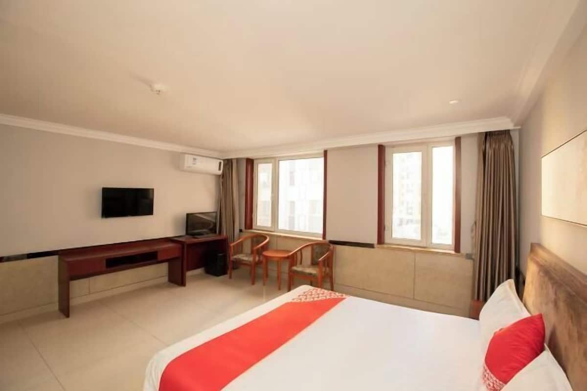 A hotel room with a bed, a desk, a chair, a television, and a window.