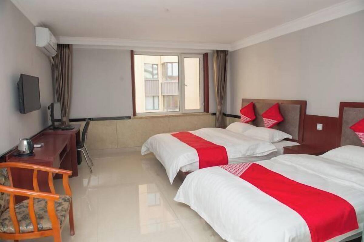 A hotel room with two beds, a desk, a chair, and a window.