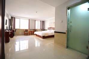 Quarto de hotel com uma cama, uma escrivaninha, uma cadeira, um guarda-roupa e uma janela grande.