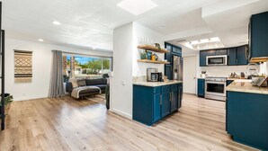 A modern kitchen with blue cabinets, a central island, and a dining area with a sofa and curtains. - Chic Spanish Palm Springs ~2000 square feet Pool Home (Palm Springs)