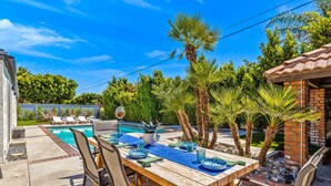 An outdoor dining area with a pool, palm trees, and a brick building. - Chic Spanish Palm Springs ~2000 square feet Pool Home (Palm Springs)