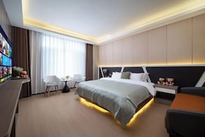 Una habitación de hotel moderna con una cama grande, un escritorio con televisor de pantalla plana, una mesita pequeña y un sillón cómodo.