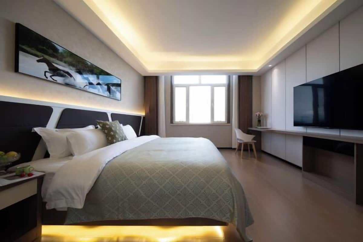 A modern hotel room with a large bed, a flat-screen TV, a desk, and a window with curtains.